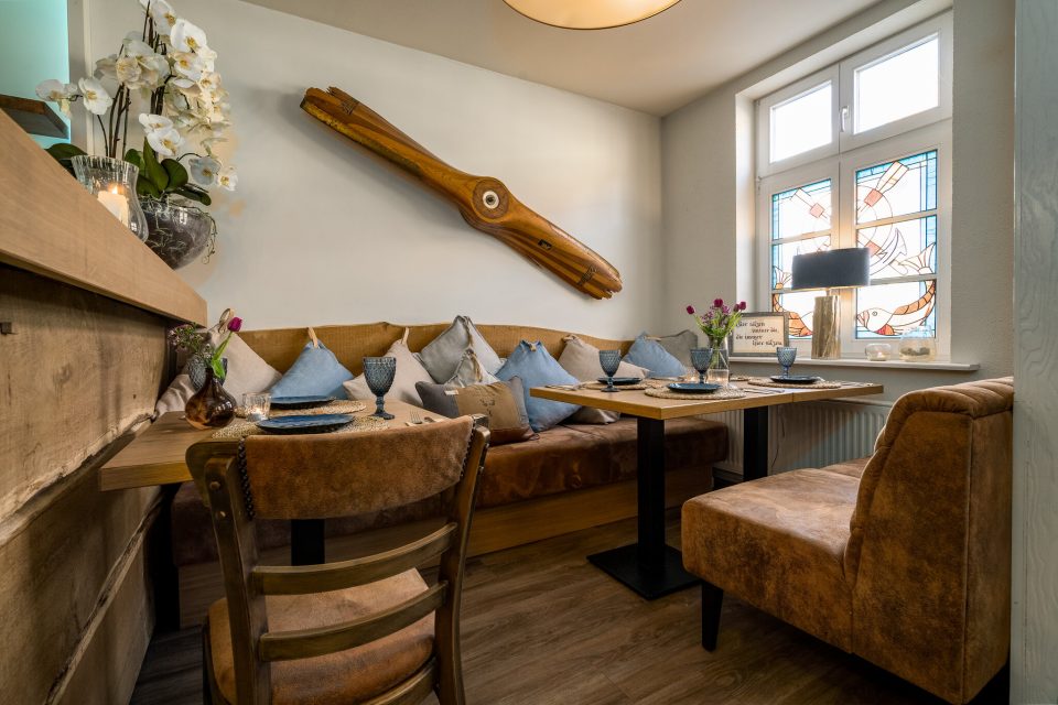 Innenraum der Blauen Maus mit Holz-Propeller an der Wand, gemütliche Sitzecke und Buntglasfenster